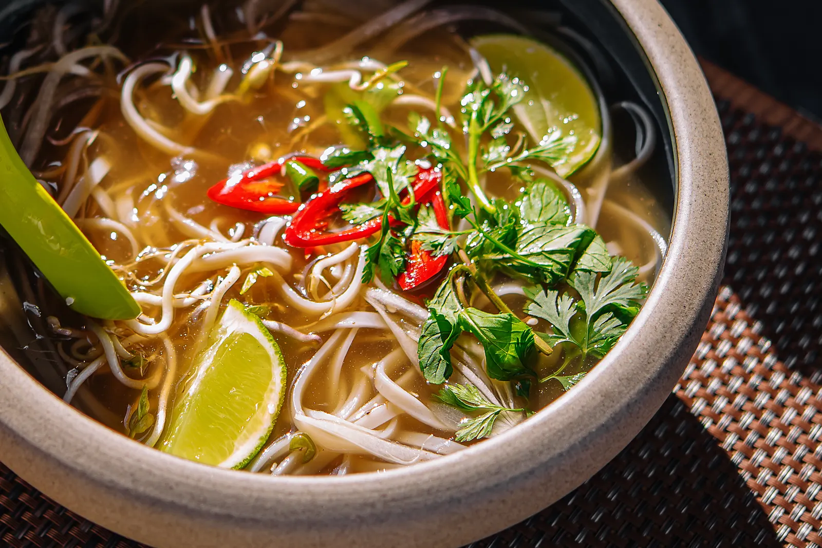 A bowl of Vietnamese noodle soup with lime, chilli and coriander